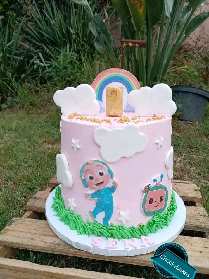 Pink celebration cake with white clouds, a rainbow and green buttercream at the base.