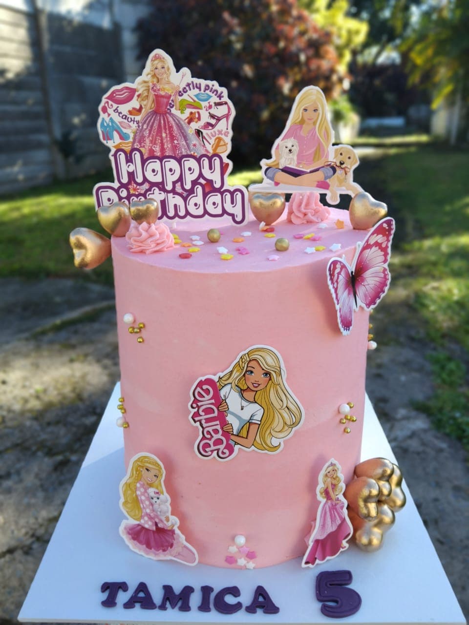 Pink birthday cake in smooth buttercream, finished with hearts and colourful toppers.