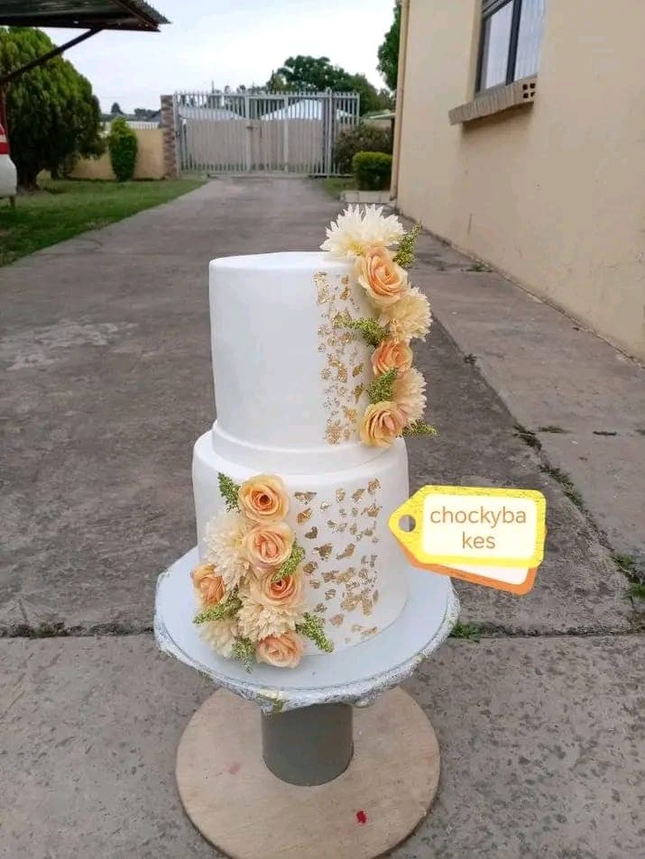 Two-tier white celebration cake with peach roses and gold leaf.