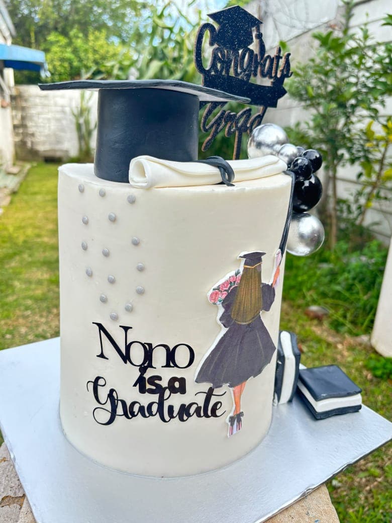 White graduation cake with a mortarboard, a scroll and black-and-silver decorations.