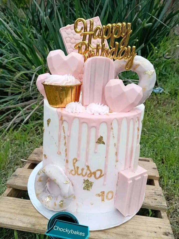 Pink and white drip celebration cake with buttercream swirls, gold leaf and a birthday topper.